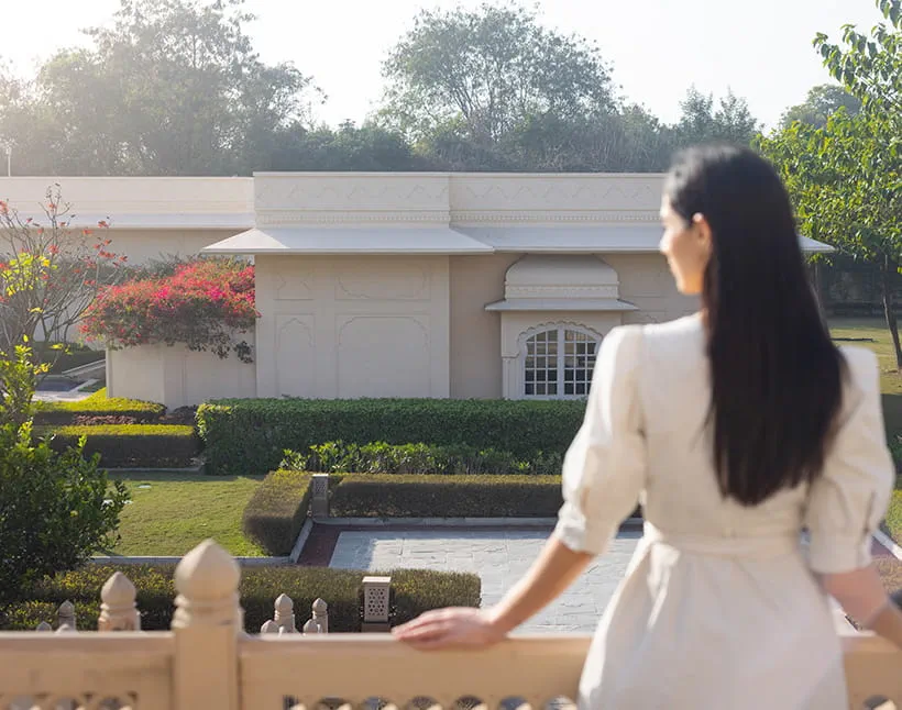 A woman overlooks The Oberoi Sukhvilas resort, surrounded by greenery.